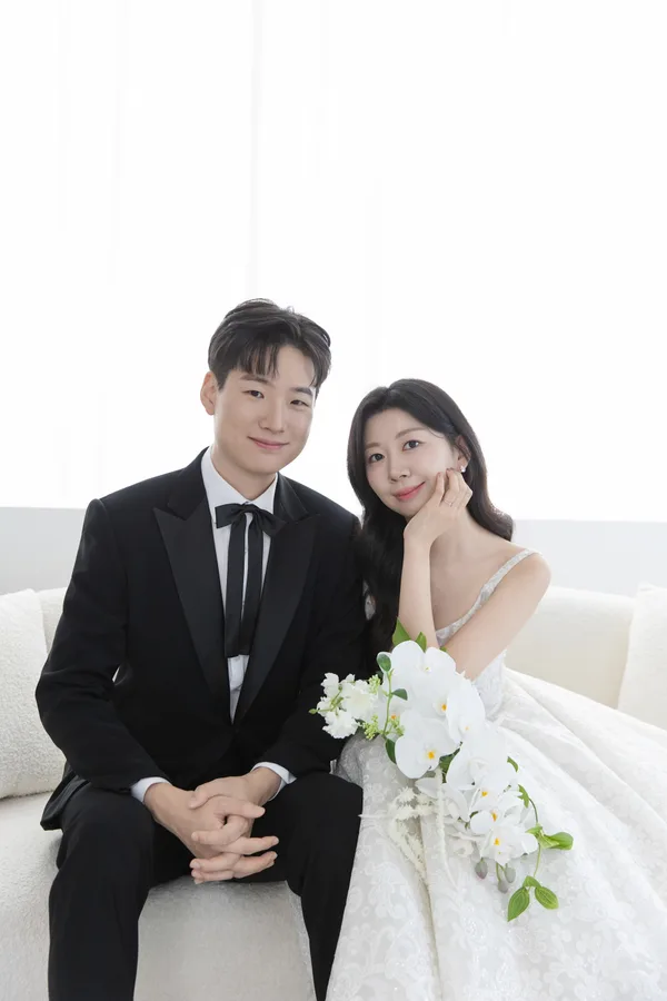 흰 소파에 함께 앉아 카메라를 바라보는 두 사람